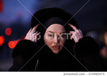 Muslim woman walking on an urban city street on a cold winter night wearing hijab 114980473
