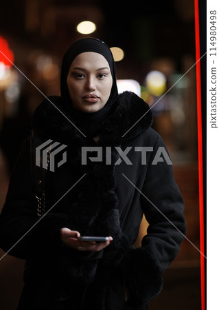 Muslim woman walking on an urban city street on a cold winter night wearing hijab 114980498