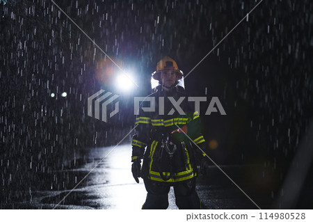 A determined female firefighter in a professional uniform striding through the dangerous, rainy night on a daring rescue mission, showcasing her unwavering bravery and commitment to saving lives. 114980528