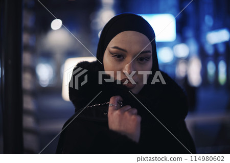 Muslim woman walking on an urban city street on a cold winter night wearing hijab Muslim woman walking on an urban city street on a cold winter night wearing hijab 114980602