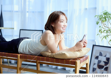 一位女士躺在房間的椅子上，看著她的智慧型手機 114980643