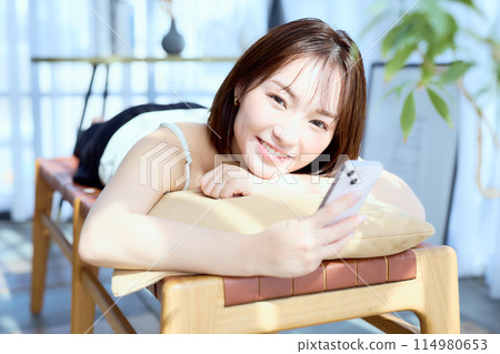 一位女士躺在房間的椅子上，看著她的智慧型手機 114980653