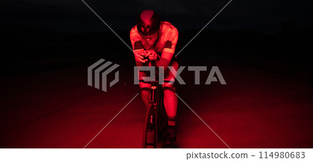 A triathlete rides his bike in the darkness of night, pushing himself to prepare for a marathon. The contrast between the darkness and the light of his bike creates a sense of drama and highlights the 114980683