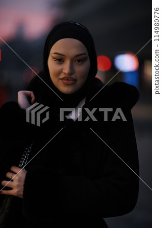 Muslim woman walking on an urban city street on a cold winter night wearing hijab Muslim woman walking on an urban city street on a cold winter night wearing hijab 114980776