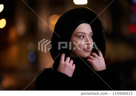 Muslim woman walking on an urban city street on a cold winter night wearing hijab 114980815