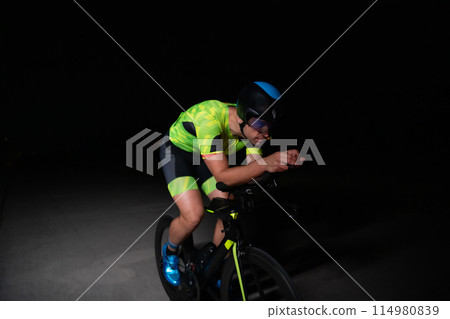 A triathlete rides his bike in the darkness of night, pushing himself to prepare for a marathon. The contrast between the darkness and the light of his bike creates a sense of drama and highlights the 114980839