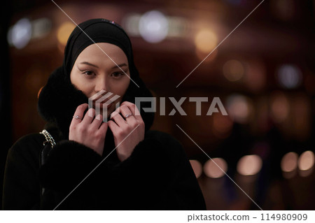 Muslim woman walking on an urban city street on a cold winter night wearing hijab Muslim woman walking on an urban city street on a cold winter night wearing hijab 114980909