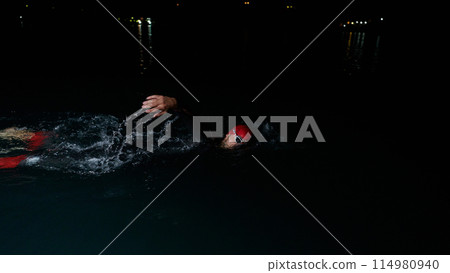 A determined professional triathlete undergoes rigorous night time training in cold waters, showcasing dedication and resilience in preparation for an upcoming triathlon swim competition 114980940