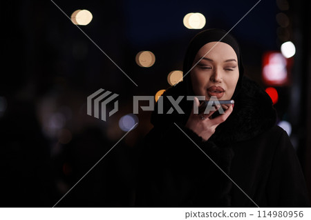 uropean Muslim Hijabi Business Lady checking her phone on urban city street at night 114980956