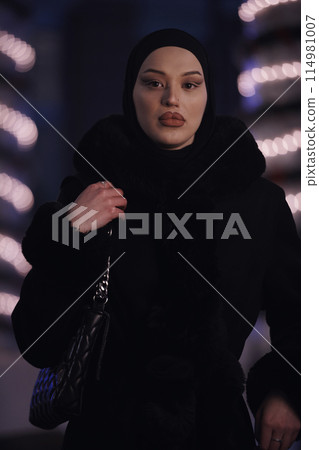 Muslim woman walking on an urban city street on a cold winter night wearing hijab Muslim woman walking on an urban city street on a cold winter night wearing hijab 114981007