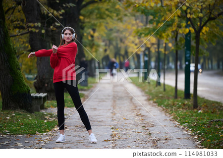 Young beautiful woman running in autumn park and listening to music with headphones on smartphone Young beautiful woman running in autumn park and listening to music with headphones on smartphone 114981033