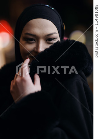 Muslim woman walking on an urban city street on a cold winter night wearing hijab 114981088