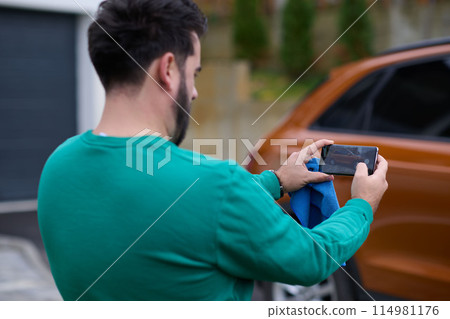 man taking photos on a smartphone of a car preparing for sale  114981176