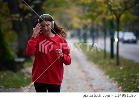 Young beautiful woman running in autumn park and listening to music with headphones on smartphone Young beautiful woman running in autumn park and listening to music with headphones on smartphone 114981180