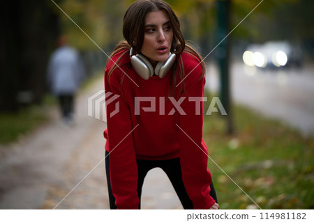 Athletic young woman taking a breath and relaxing after jogging and stretching. Woman Training and Workout Exercises On Street. Athletic young woman taking a breath and relaxing after jogging and stretching. Woman Training and Workout Exercises On Street. 114981182
