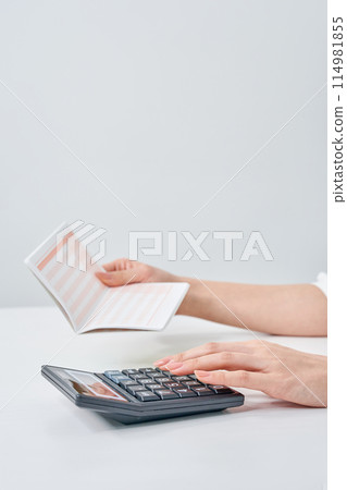 A woman using a calculator with a bank account passbook in her hand A woman using a calculator with a bank account passbook in her hand 114981855