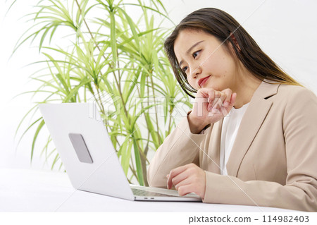 一位年輕的女商人在辦公桌前工作，同時在辦公室思考 114982403