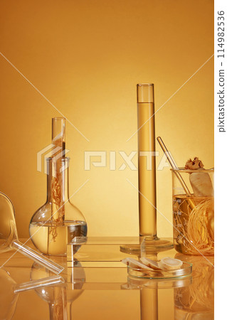 Yellow background photo with frontal shot has ginseng composition and lab instruments including measuring cylinder, boiling flask, beaker, petri dish and a blank glass showcase podium in center Yellow background photo with frontal shot has ginseng composition and lab instruments including measuring cylinder, boiling flask, beaker, petri dish and a blank glass showcase podium in center 114982536