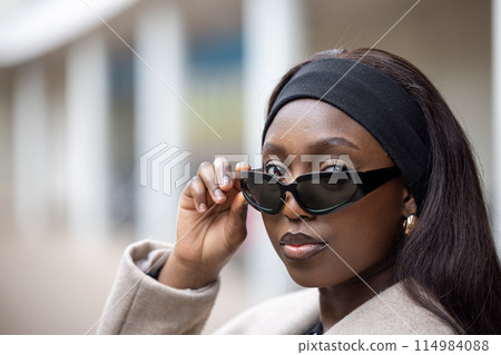 Stylish woman poses in urban setting with chic style, sunglasses adding to her confidence Stylish woman poses in urban setting with chic style, sunglasses adding to her confidence 114984088