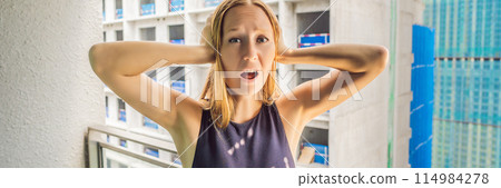 Young woman on the balcony annoyed by the building works outside. Noise concept. Air pollution from building dust BANNER, LONG FORMAT Young woman on the balcony annoyed by the building works outside. Noise concept. Air pollution from building dust BANNER, LONG FORMAT 114984278