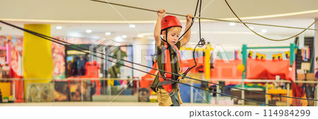 Adorable little boy enjoying his time in climbing adventure park in the mall BANNER, LONG FORMAT 114984299