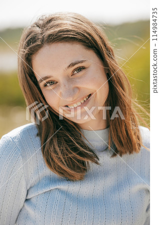 Sunlit Smile: Portrait of a Young Woman in a Blue Sweater 114984735