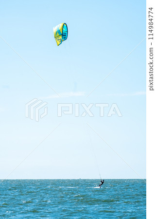 A person enjoying kiteboarding on a sunny day, gliding over the blue ocean waters 114984774