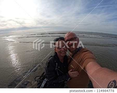 A couple smiles happily while taking a picture together at the sunny beach shore 114984778