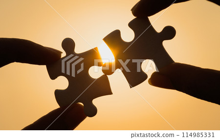 Silhouette of close up hand connecting a piece of jigsaw puzzle over sunlight effect. symbol of association,success and connection concept. business strategy. 114985331