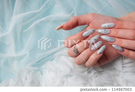 Female hands with blue nail design on blue silk background. 114987003