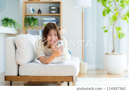 A young woman operating a smartphone in a room 114987362