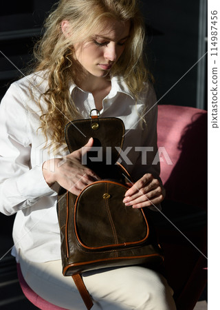 beautiful curly blond hair woman posing with a leather backpack 114987456