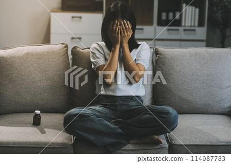 Upset woman frustrated by problem with work or relationships, sitting on couch, embracing knees, covered face in hand, feeling despair and anxiety, loneliness, having psychological trouble 114987783