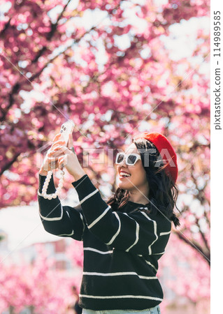 happy woman taking selfie on the phone in front of blooming sakura happy woman taking selfie on the phone in front of blooming sakura 114989585