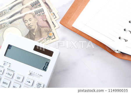 An open calculator on a desk, a ring-type system organizer, and a 10,000 yen note with a portrait of Fukuzawa Yukichi 114990035