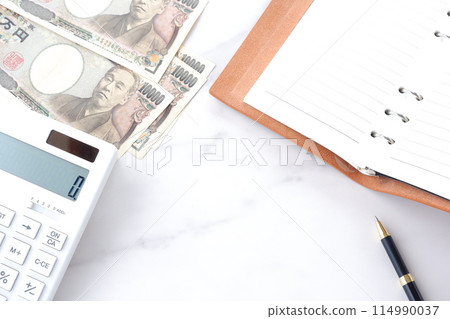 An open calculator on a desk, a ring-type system organizer, and a 10,000 yen note with a portrait of Fukuzawa Yukichi 114990037