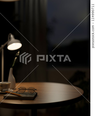 A close-up image of a round wooden tabletop featuring objects in a dark room at night. A close-up image of a round wooden tabletop featuring objects in a dark room at night. 114990711
