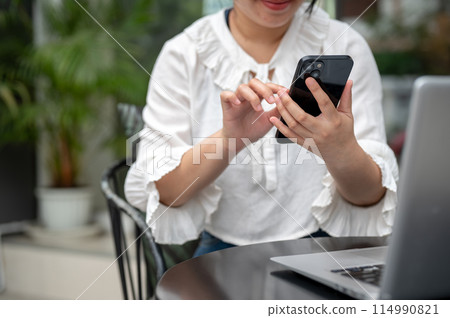 A woman is working remotely from a cafe, sitting at an outdoor table and using her smartphone. A woman is working remotely from a cafe, sitting at an outdoor table and using her smartphone. 114990821