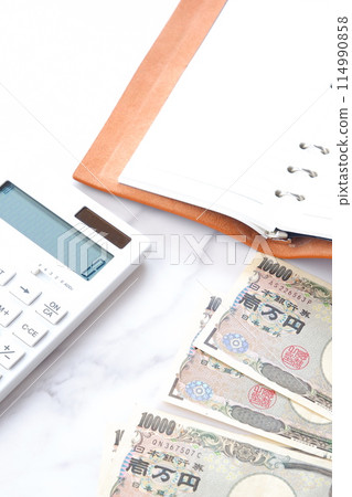 A ring-type system organizer, a calculator, and a 10,000 yen note with a portrait of Yukichi Fukuzawa on a desk 114990858