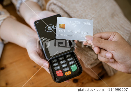 A close-up image of a customer tapping her credit card with a payment terminal in a clothing store. 114990907
