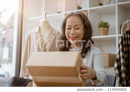 A happy mature Asian female online seller holding a cardboard box, proud of her online business. A happy mature Asian female online seller holding a cardboard box, proud of her online business. 114990983