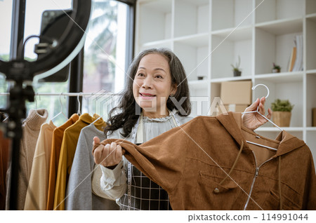 A female online seller is showing her goods live on her social media, selling clothes online. A female online seller is showing her goods live on her social media, selling clothes online. 114991044