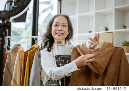 A female online seller is showing her goods live on her social media, selling clothes online. A female online seller is showing her goods live on her social media, selling clothes online. 114991045