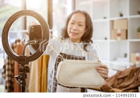 A selective focus image of a smartphone on an LED ring light with a seller selling her goods online. A selective focus image of a smartphone on an LED ring light with a seller selling her goods online. 114991051