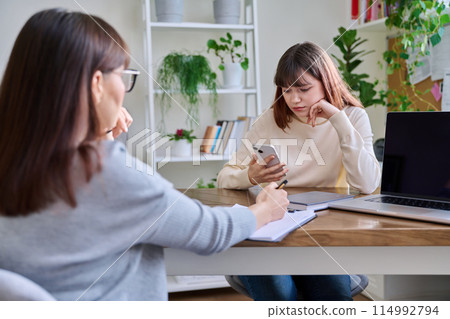 Sad teenage girl talking to psychotherapist at therapy session in office 114992794