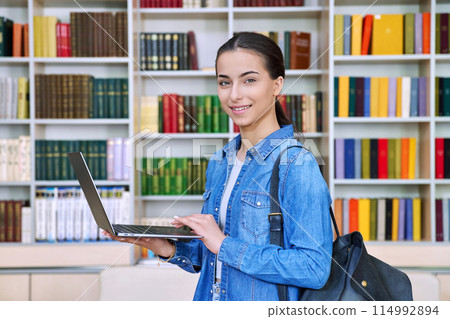 Teenage girl student using laptop, inside high school building, in library Teenage girl student using laptop, inside high school building, in library 114992894