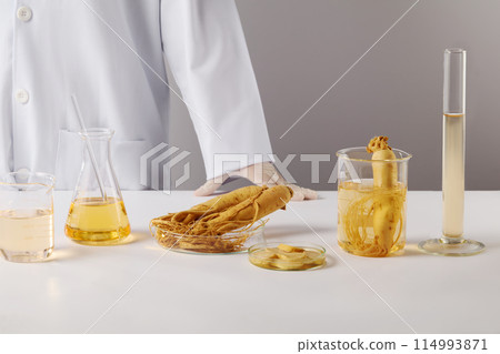 Laboratory and ginseng theme photo with frontal shot on white background, experiment tools neatly arranged on a white countertop with a scientist stand in back. Space for text and displaying product 114993871