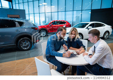 Happy caucasian couple signs a contract for the purchase of a car salon. 114994312