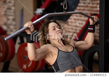 Caucasian forty-year-old woman doing lat pull-downs in the gym. 114994313