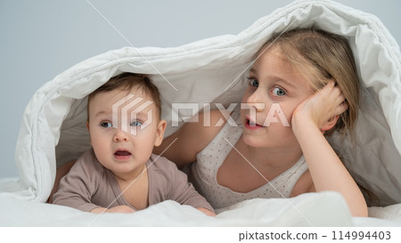 Little girl and her newborn brother hiding under the blanket.  114994403